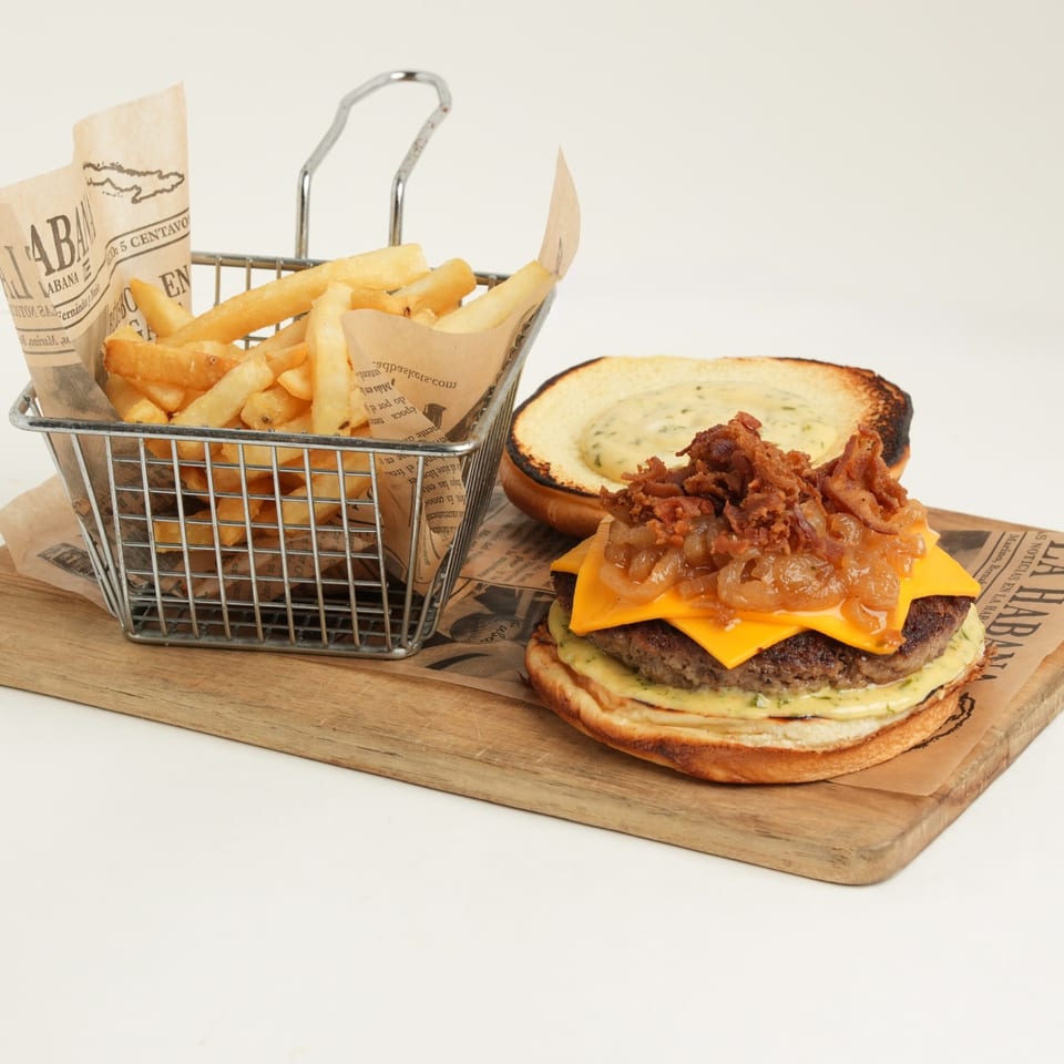 Cheeseburger topped with caramelized onions and crispy fried onions beside a basket of golden fries on a wooden board.