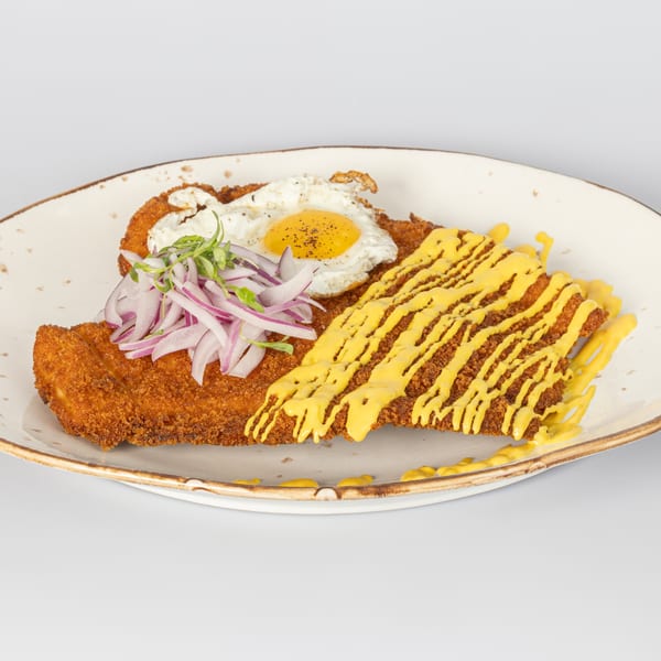 Two crispy fried chicken cutlets, one topped with a fried egg and red onions, the other with yellow sauce.