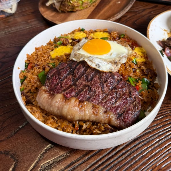 Grilled steak and a sunny-side-up egg on a bed of Latin-American fried rice in a white bowl.