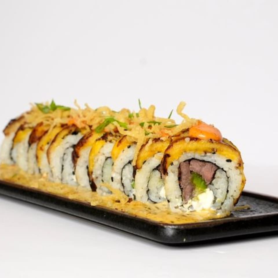 Sliced sushi roll topped with crispy tempura flakes, drizzled sauce, and green garnish on a black rectangular plate.