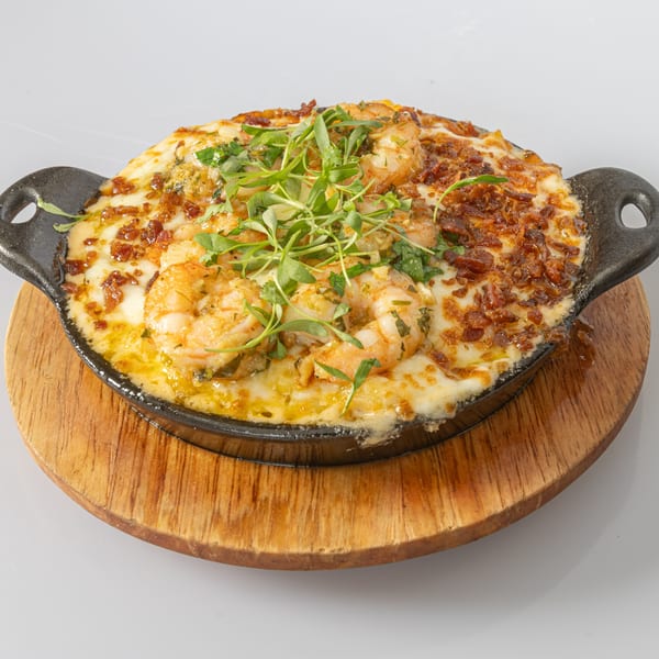Bocas House's cheesy shrimp dish with crispy bacon bits and fresh herbs in a cast iron skillet.