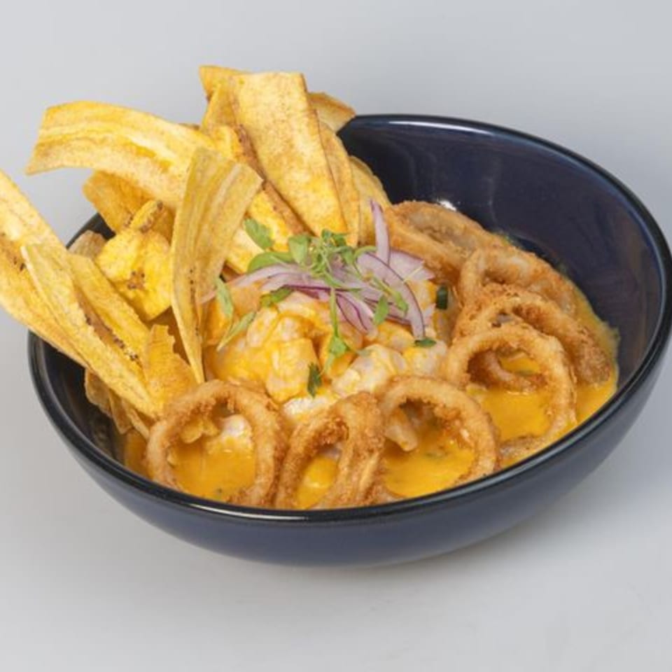 Loaded black bowl of golden cheese sauce topped with tortilla chips, onion, herbs, and crispy onion rings.