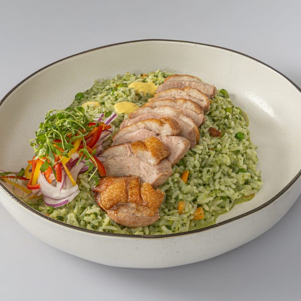 Sliced duck breast with crispy skin, served over green rice with microgreens and colorful peppers.