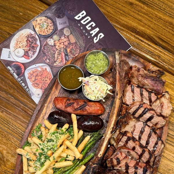 A large platter of grilled meats, sausages, fries, asparagus, and sauces from Bocas House.
