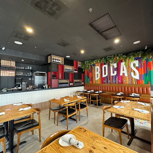 The interior of Bocas House restaurant, featuring wooden tables, a bar, and a colorful 'BOCAS HOUSE' sign.