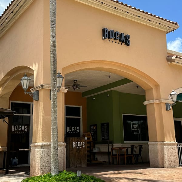 Exterior of Bocas House restaurant with a large archway entrance, palm tree, and green walls.