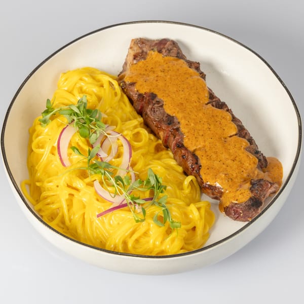 Bocas House's steak with orange sauce next to yellow pasta, garnished with red onions and greens.