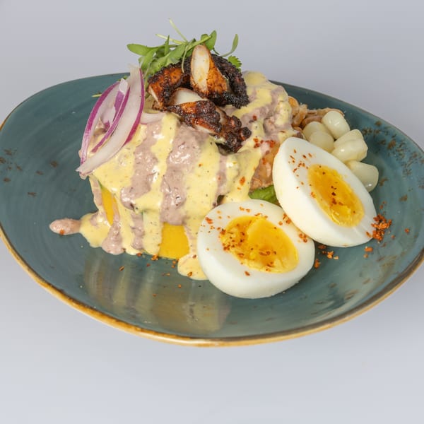 Bocas House's Latin-American dish with octopus, red onion, corn, and hard-boiled eggs on a blue plate.