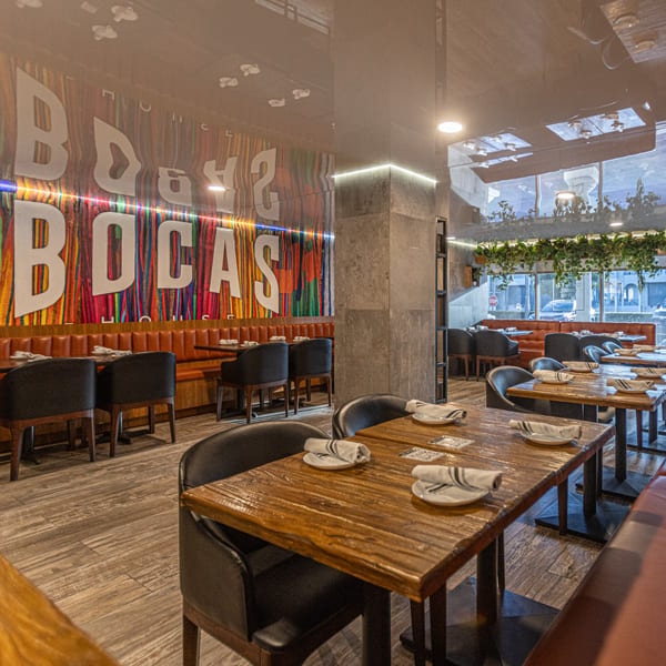 Interior of Bocas House restaurant with wooden tables, black chairs, and a colorful mural on the wall.