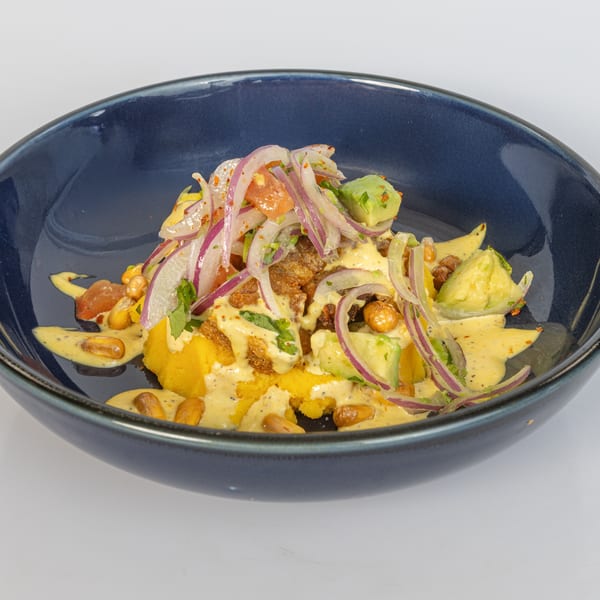 Bocas House Latin-American dish with yellow puree, red onions, avocado, and a creamy sauce in a blue bowl.