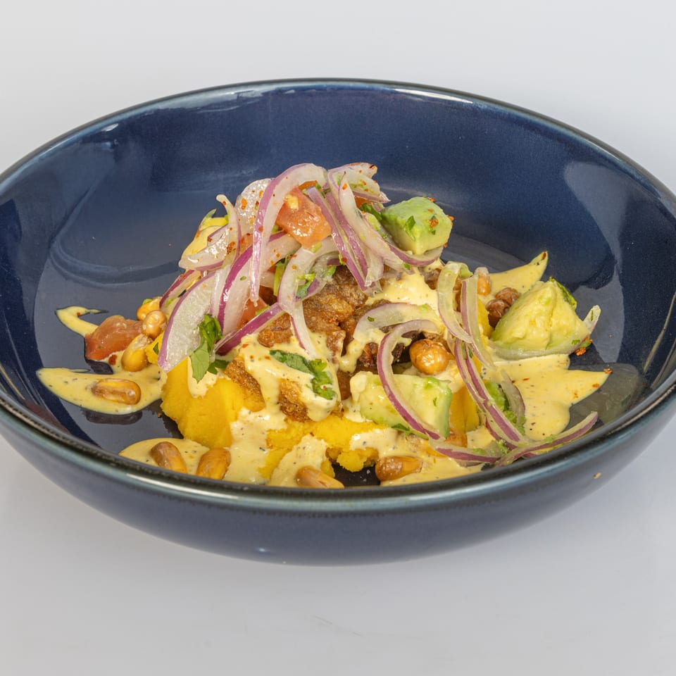 Bocas House Latin-American dish with yellow puree, red onions, avocado, and a creamy sauce in a blue bowl.