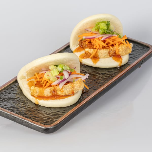 Two Bocas House bao buns with fried tofu, shredded carrots, red onions, and scallions on a black plate.