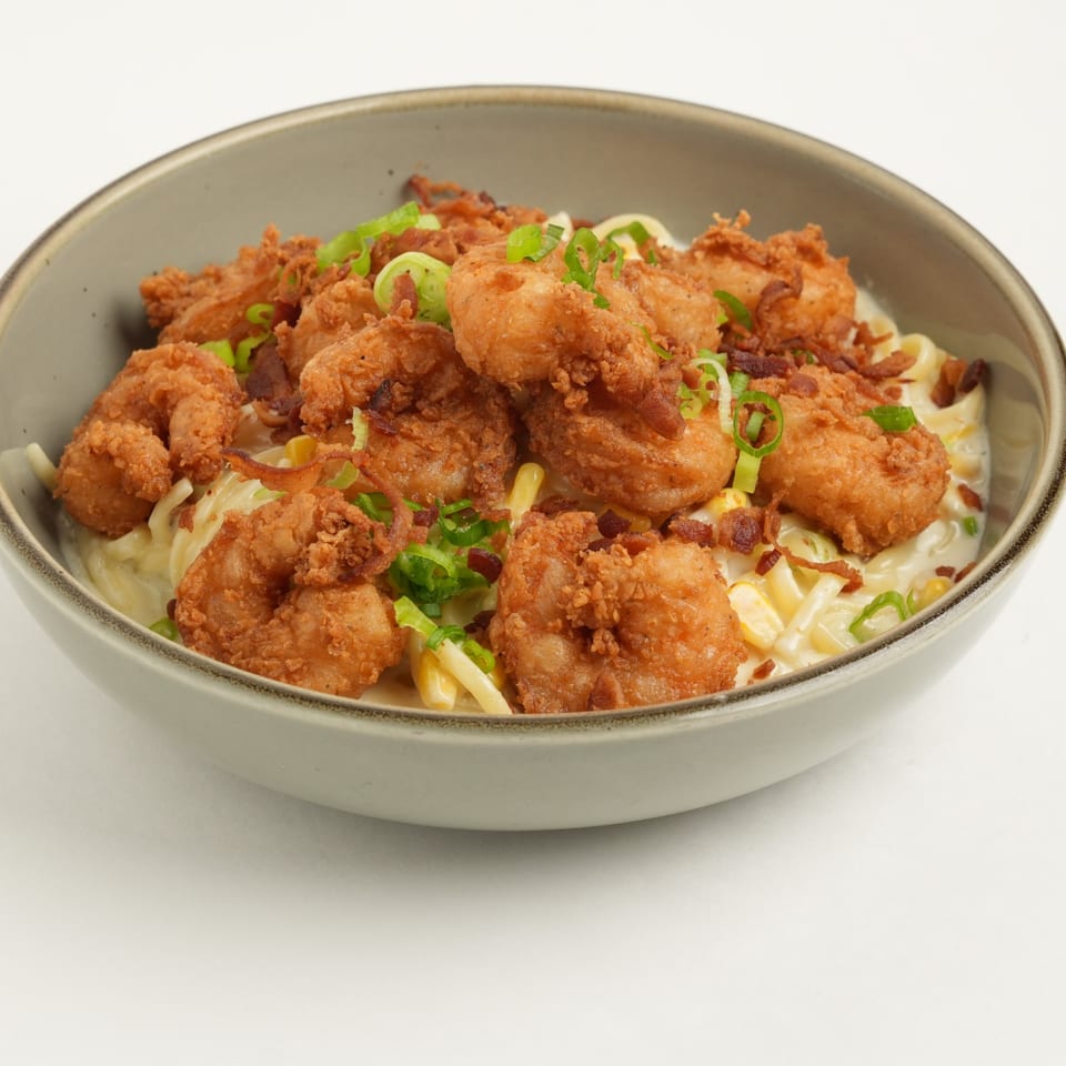 Crispy fried chicken pieces topped with green onions and fried onions over creamy pasta in a ceramic bowl.