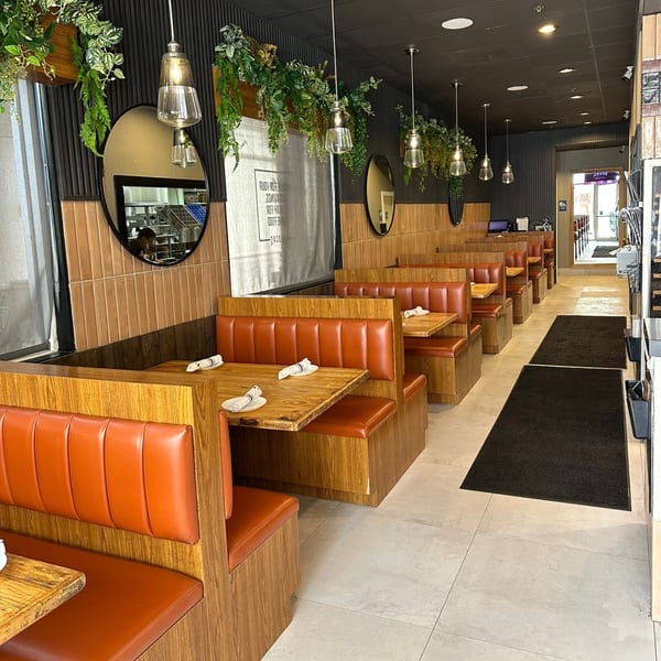 Bocas House dining room with orange booths, wooden tables, hanging plants, and modern pendant lights.