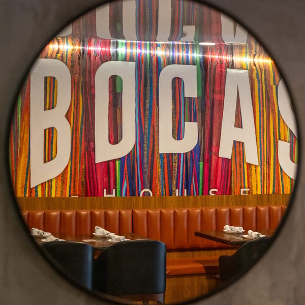 Bocas House restaurant interior with a colorful striped wall featuring the "BOCAS HOUSE" logo and brown booths.