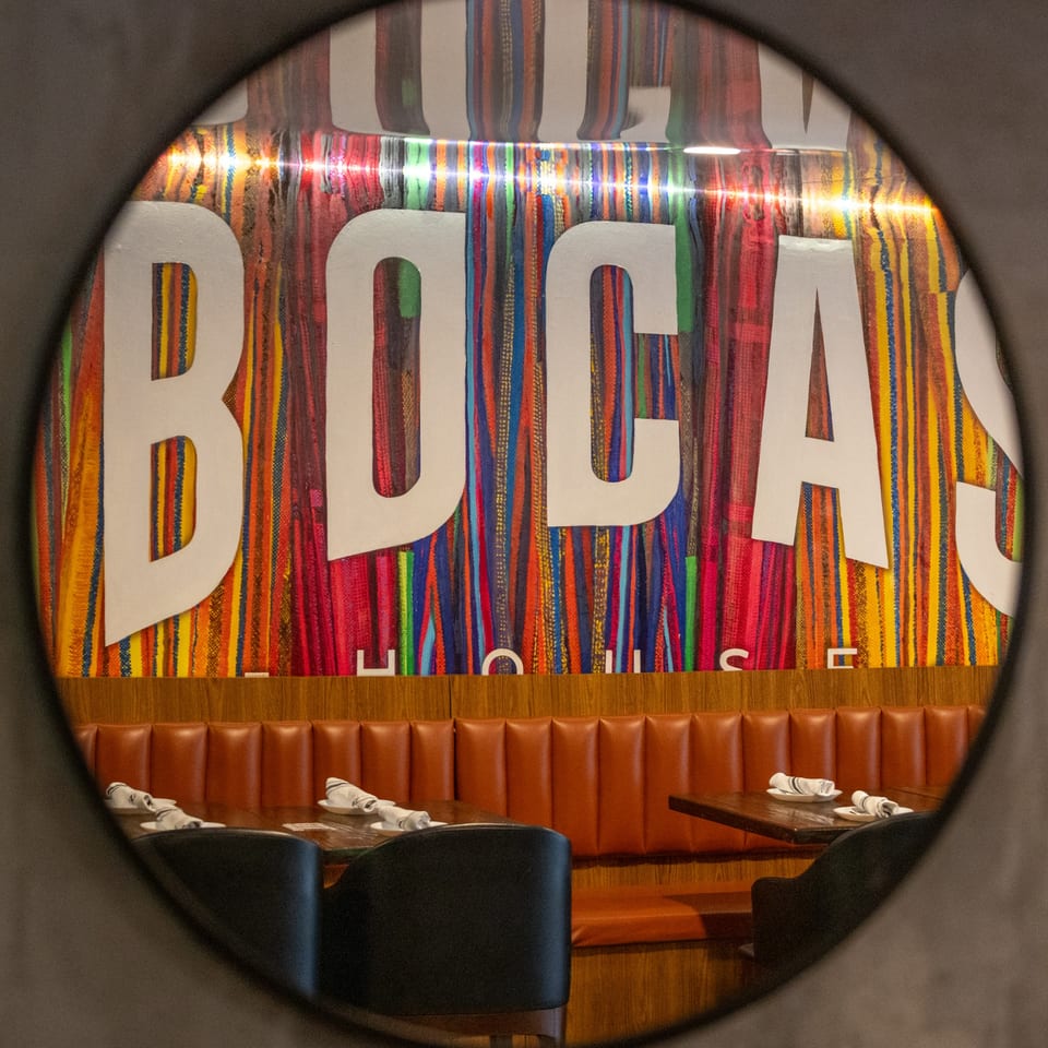 Bocas House restaurant interior with a colorful striped wall featuring the "BOCAS HOUSE" logo and brown booths.
