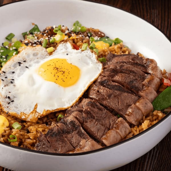 Bocas House's Latin-American dish with sliced steak, fried egg, rice, and green onions in a white bowl.