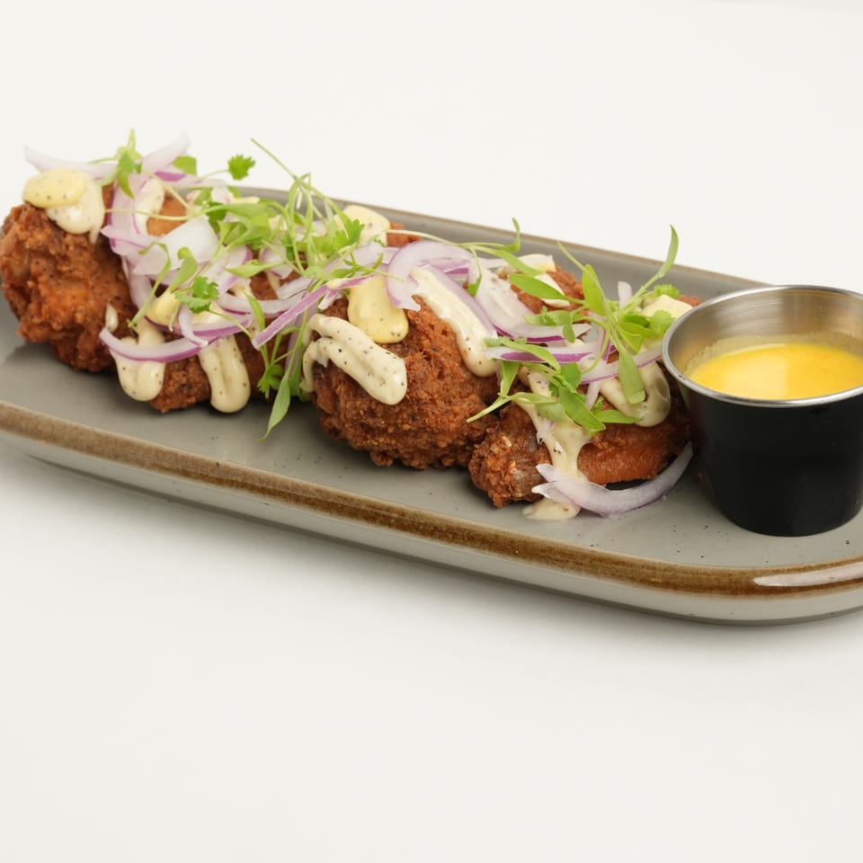 Crispy falafel patties topped with creamy sauce, red onion, and microgreens, served with yellow dipping sauce on a platter.